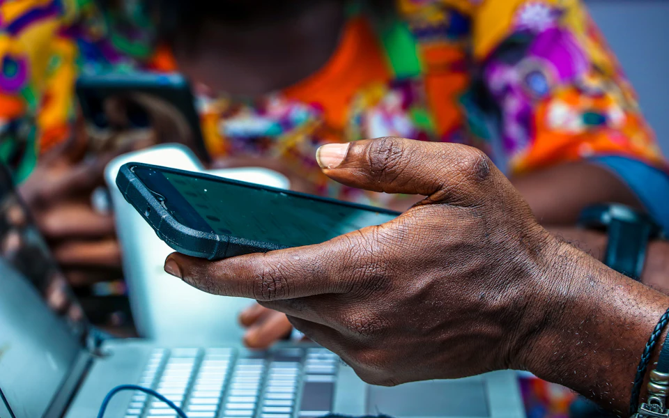 Close-up of hands holding a phone over a laptop